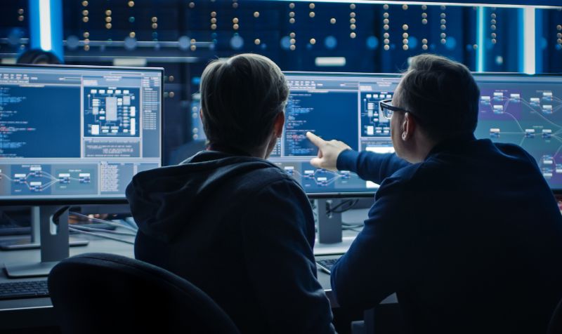  Two Professional IT Programers Discussing Blockchain Data Network Architecture Design and Development Shown on Desktop Computer Display. 